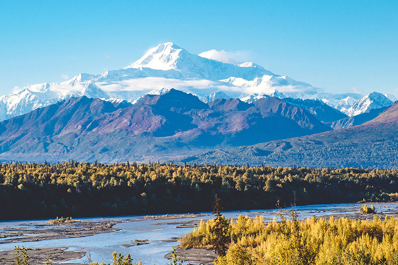 A mountain landscape with river in foreground and blue sky
