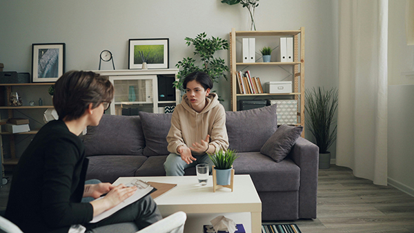 A young person sits on a couch talking with a counselor 